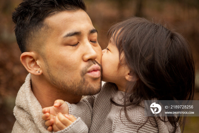 Close-up of loving cute daughter kissing father on cheek in forest