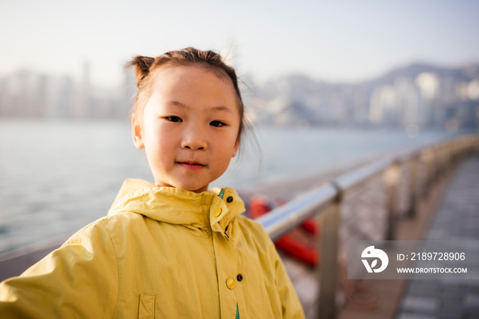 Portrait of young girl wearing yellow coat in front of water looking at camera