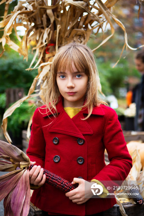 Portrait of girl holding red sweetcorn while standing in market