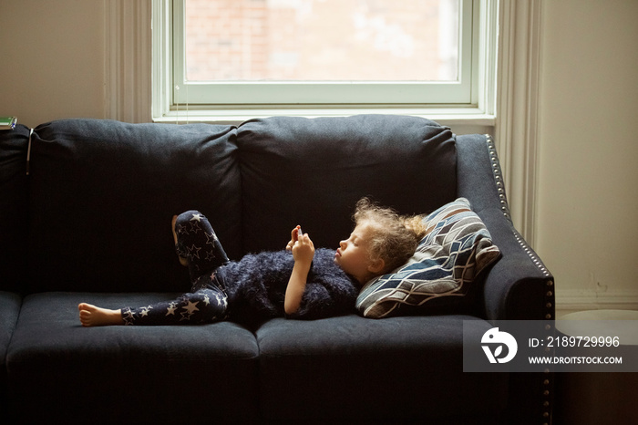 Side view of cute girl using smart phone while lying on sofa at home