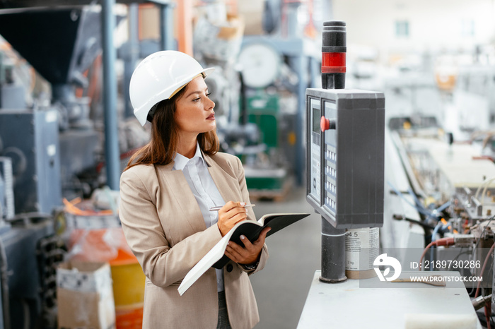 Portrait of businesswoman in factory. Young female architect with helmet in suit.