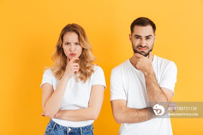 Image of irritated couple man and woman frowning and touching their chins while looking at camera