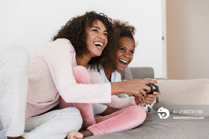 Image of american woman and little girl playing video games with joysticks