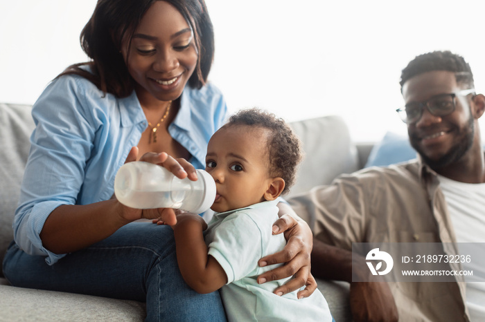 Happy African American mom feeding child from bottle