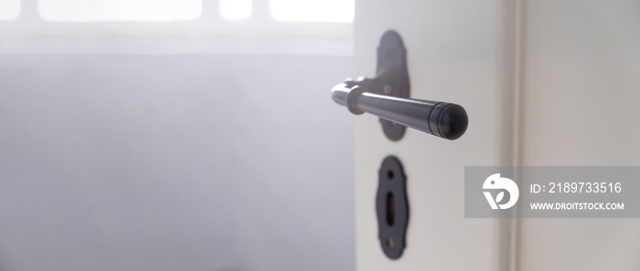 Door open close up view. Retro black doorknob and key lock on white wooden door, blur room interior