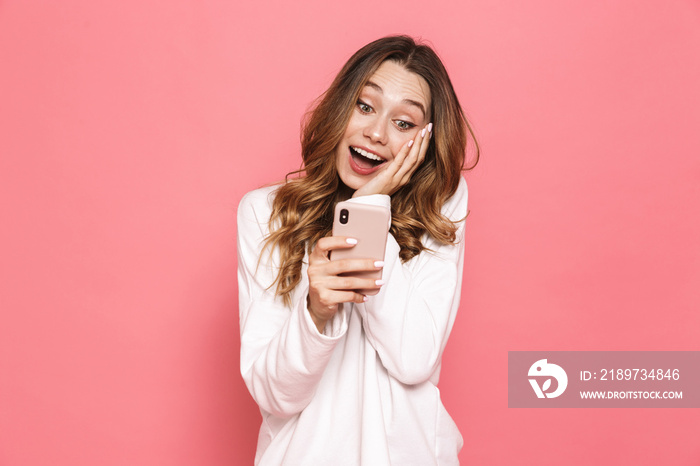 Image of surprised brunette woman with beautiful long hair holding cell phone in hands, isolated ove