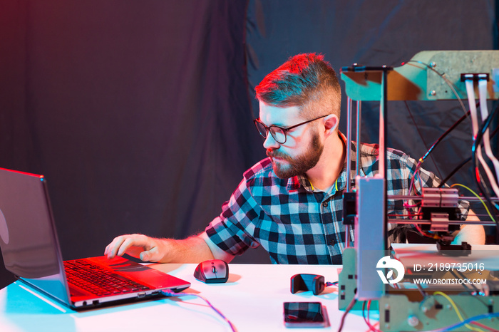 Young male designer engineer using a 3D printer in the laboratory and studying a product prototype, 