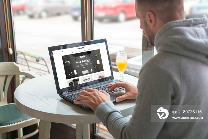 Visitor open a responsible website of the design company on his laptop. Coffee shop in background.