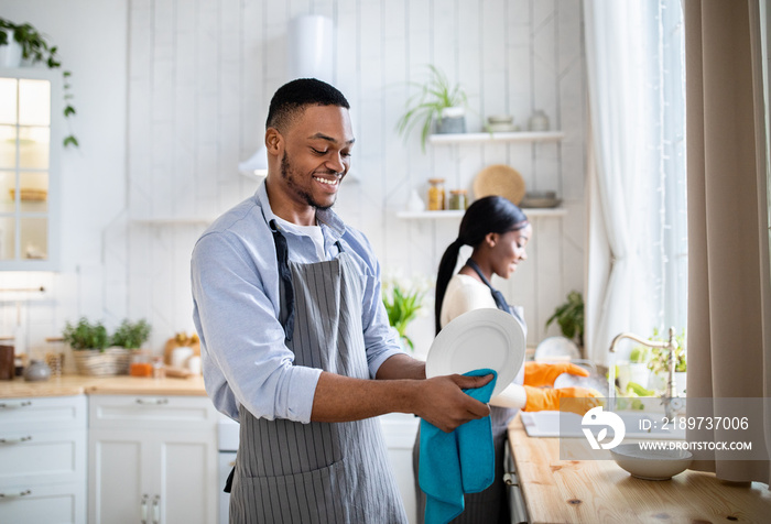 Cheerful black woman washing dishes while her husband wiping them at kitchen, copy space