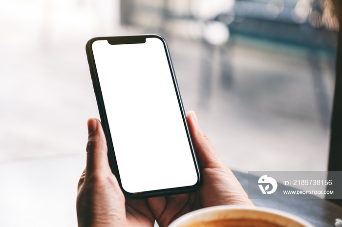 Mockup image of a woman holding black mobile phone with blank screen with coffee cup on the table