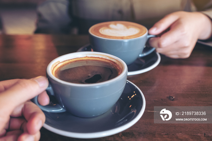 Close up image of a man and a woman clinking blue coffee mugs on wooden table in cafe