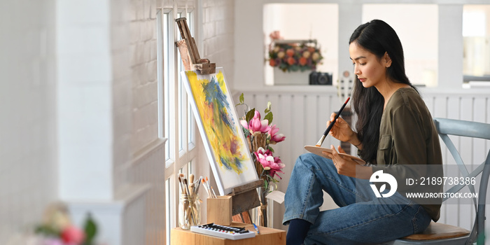 美丽的女人坐在椅子上用画笔在画布上画画，既现代又舒适