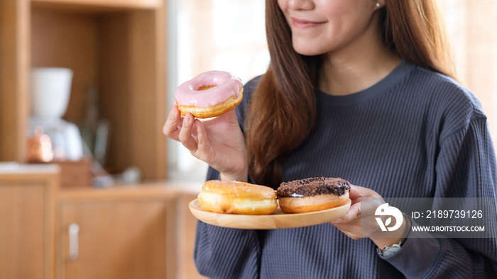 Closeup image of a young woman holding and enjoyed eating donuts at home