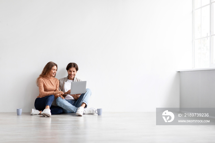 Glad young caucasian male and female sitting on floor, rest, planning new interior at computer in em