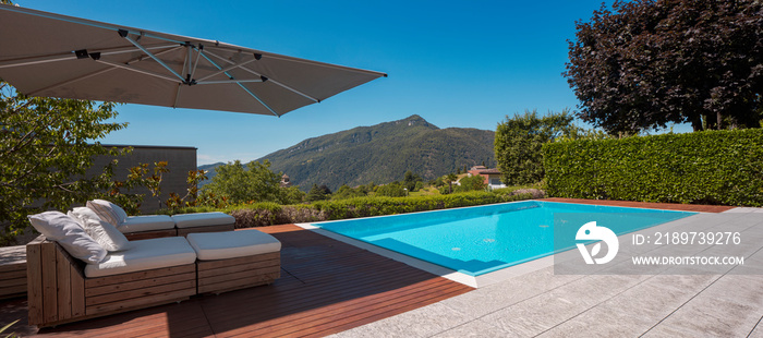 大型现代化游泳池，配有两个日光浴躺椅和一把遮阳伞。山景o
