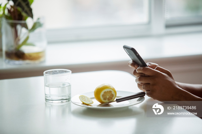 Cropped image of woman using mobile phone by drinking glass and sliced lemon at table