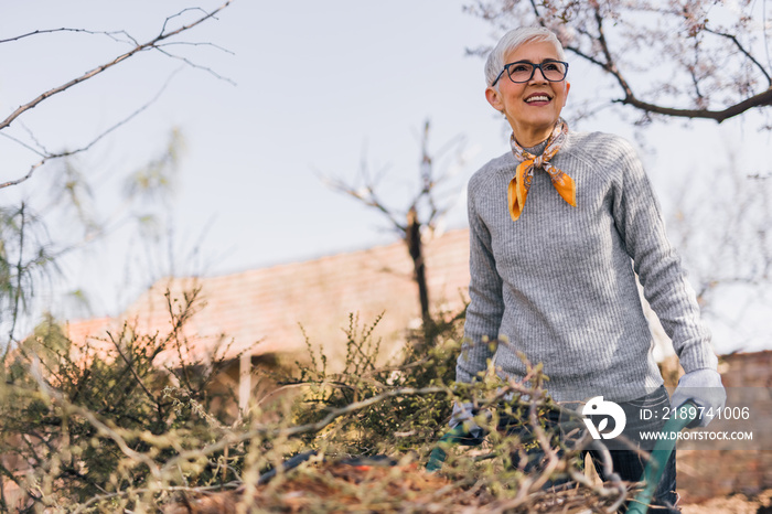 Happy senior woman working in the garden, doing spring cleaning.