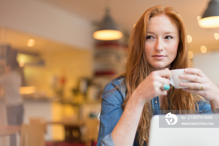 Young woman drinking coffee and working at laptop in cafe