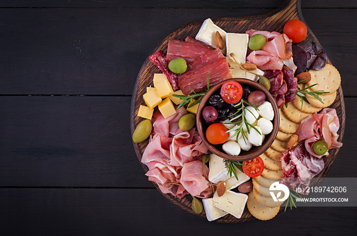 Antipasto platter with ham, prosciutto, salami, cheese,  crackers and olives on a wooden background.