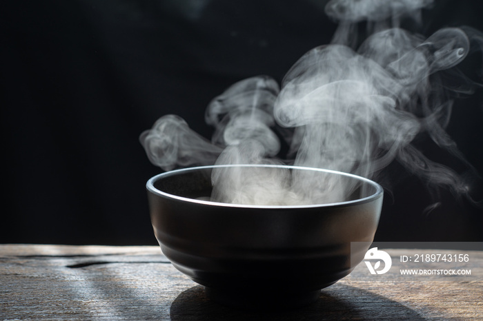 在黑暗的背景上用烟熏木碗蒸热汤。选择性聚焦