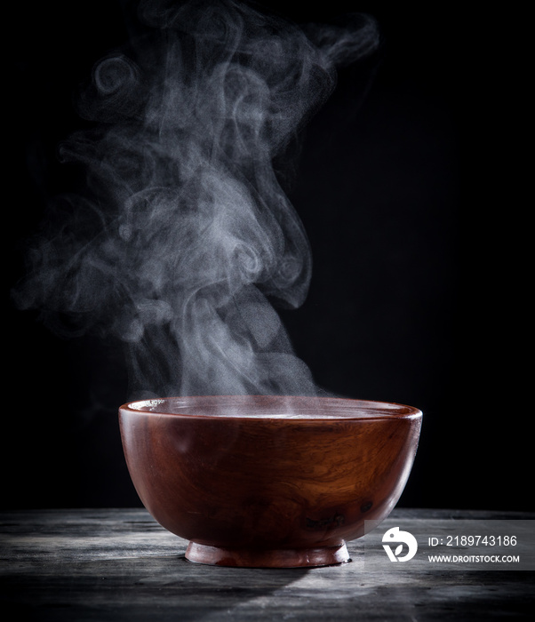 Steam of hot soup in a soup bowl with smoke on black background