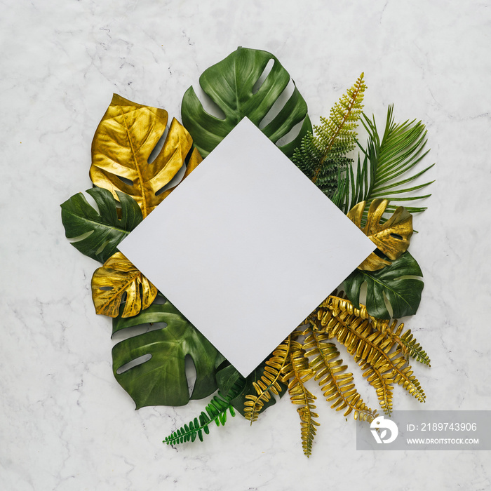 Top view of green and gold tropical leaves on white marble background. Flat lay. Minimal summer conc