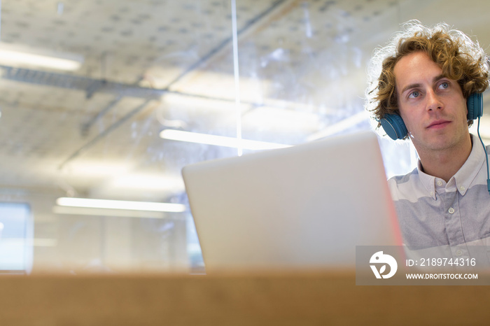 Businessman with headphones working at laptop in office