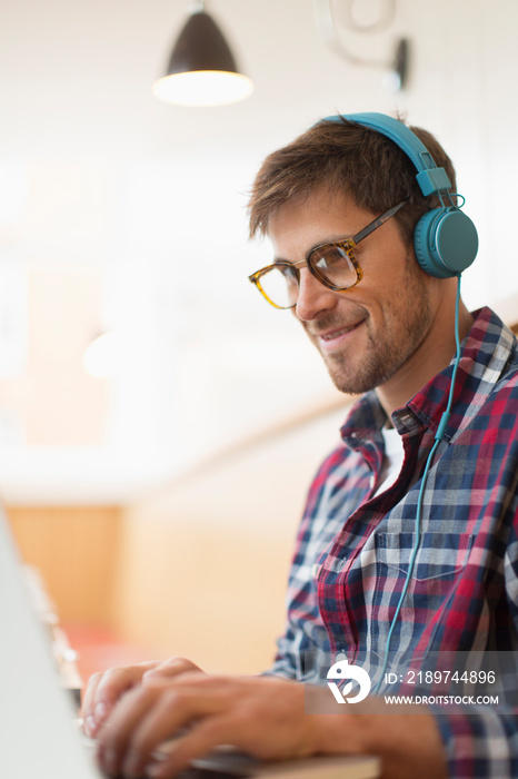 Smiling man with headphones working at laptop in cafe