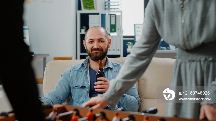 Portrait of businessman holding bottle of beer after work at office. Person looking at colleagues pl