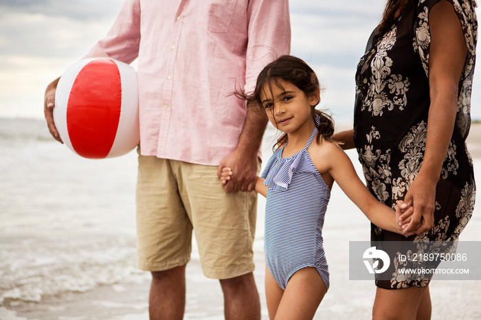 Girl (6-7) holding hands with parents on beach