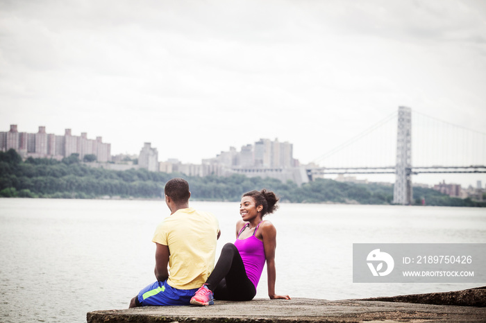 Couple in sports clothing sitting on riverbank