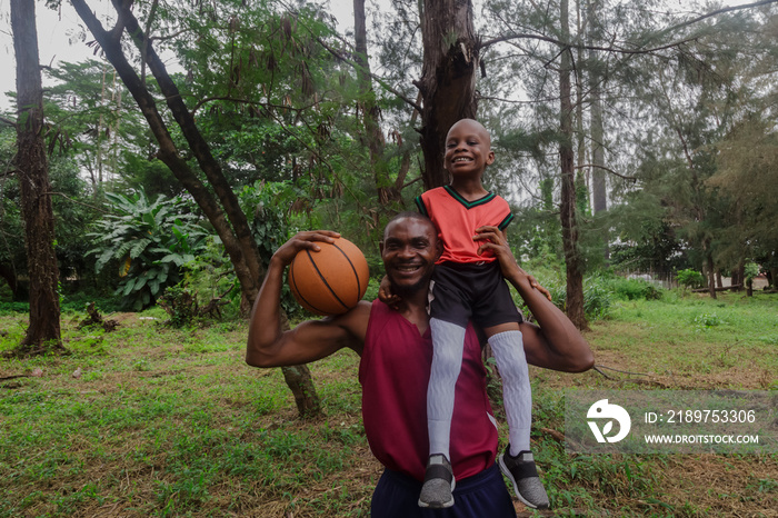 Father carry son on shoulder while holding basketball at the park