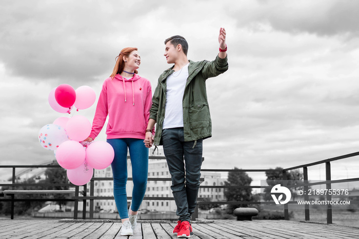 Walking and talking. Cheerful relaxed young girl holding a bunch of pink balloons while walking on t