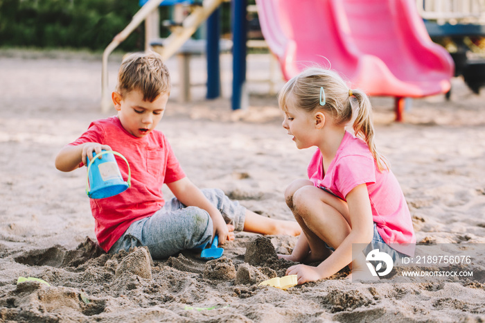 Two Caucasian children sitting in sandbox playing with beach toys. Little girl and boy friends havin