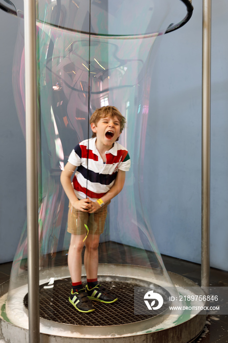 Little blond kid boy playing with huge soap bubbles construction indoors. Happy healthy smiling chil