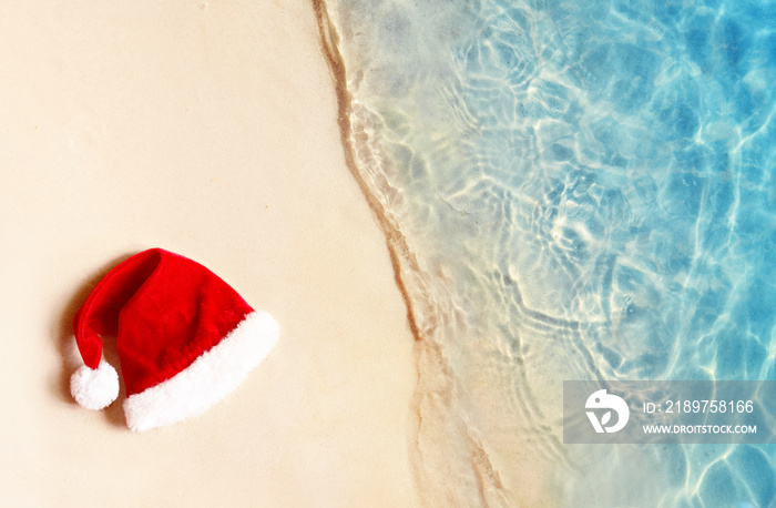 Christmas holidays concept. Top view of santa claus hat on summer sand beach.