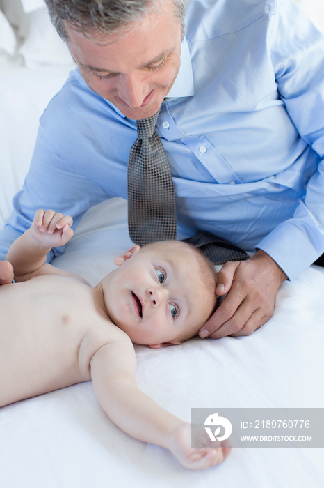 Father watching cute baby son on bed