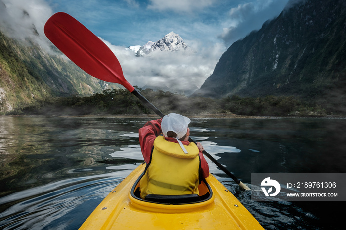 Young boy in bright yellow kayak on mountain lake. White mountain peak in the background