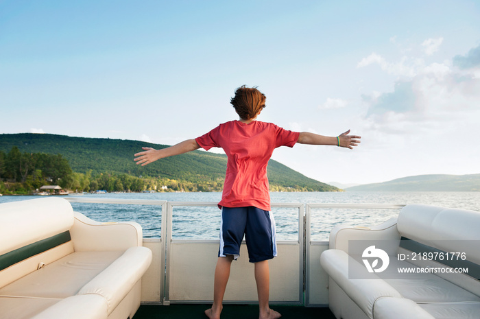 Boy (12-13) standing on boat with arms outstretched