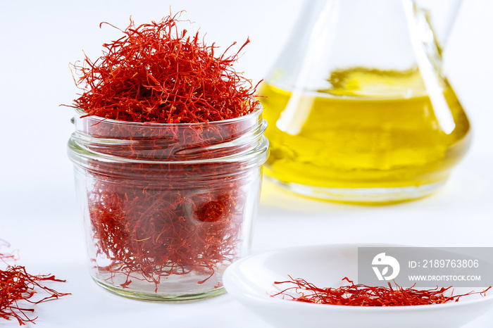 Dried saffron threads in a glass bottle and oil extract on a white background.