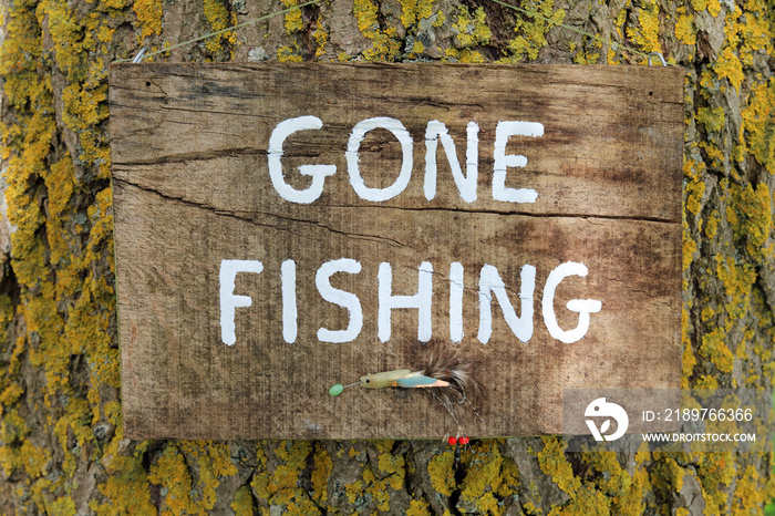 gone fishing sign written a wooden plaque hanging on a tree