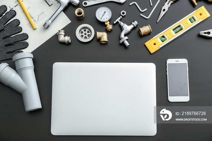 Modern laptop, mobile phone and plumbing items on dark background