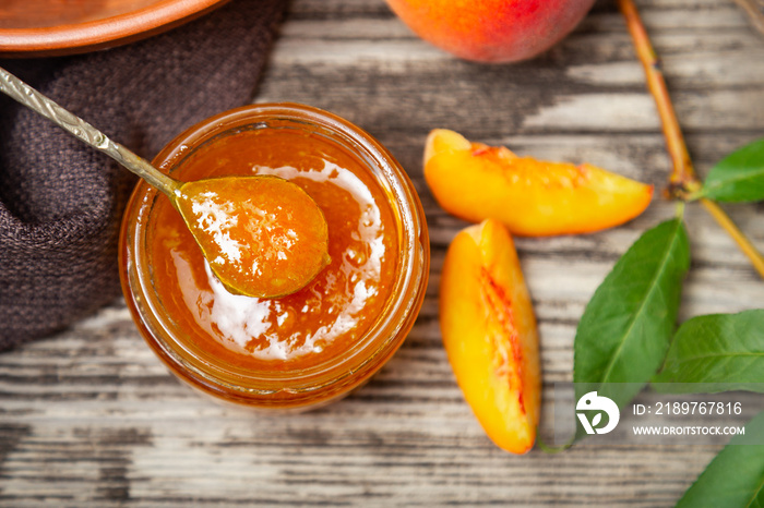 Peach jam in glass jar with peach wedges and whole peach fruit. Peach jam on wooden table. Top view