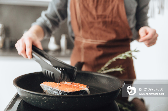 Young lady standing in kitchen while cooking fish.