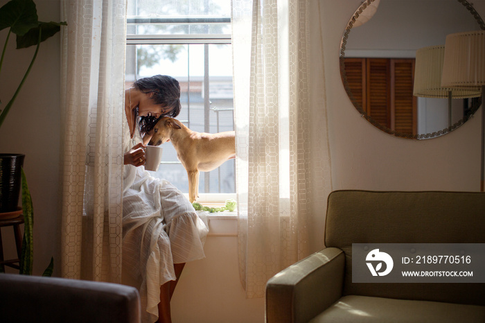 Woman playing with her dog while sitting on window sill