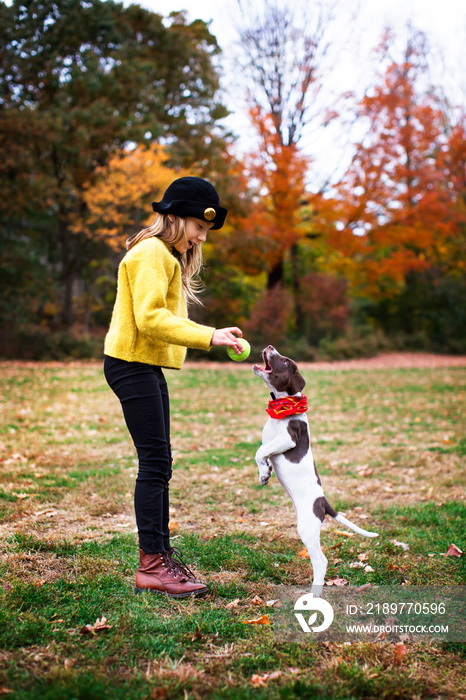 Girl holding ball playing with dog in park during autumn