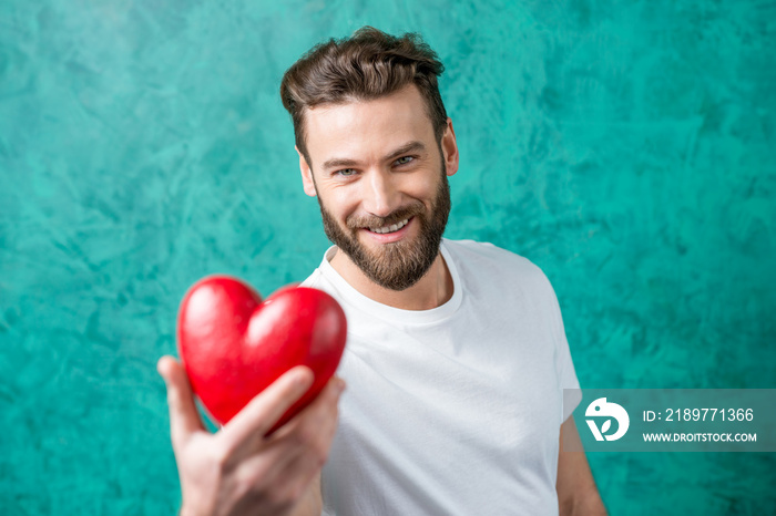 Handsome man in the white t-shirt giving red heart standing on the painted green wall background. Va