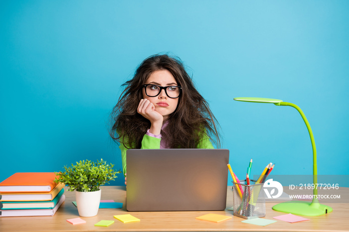 Portrait of bored high school girl sit desk look copyspace wear green shirt isolated over blue color