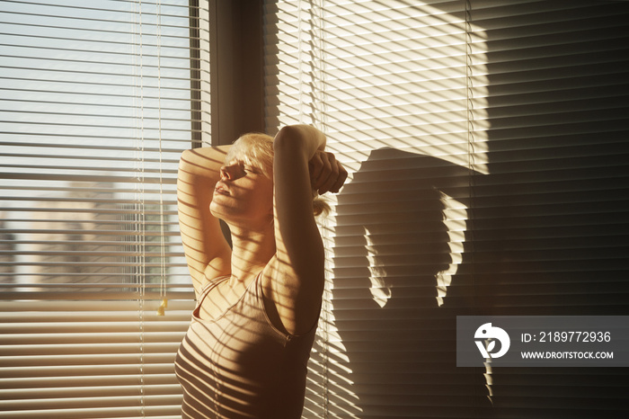 阳光下，手留头发的女人站在百叶窗旁