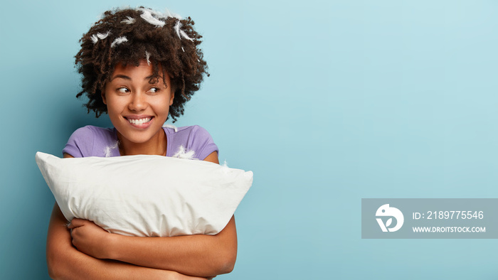 照片中，一个快乐的深色皮肤非裔美国女孩兴高采烈地看着一旁，拥抱着白色柔软的枕头。